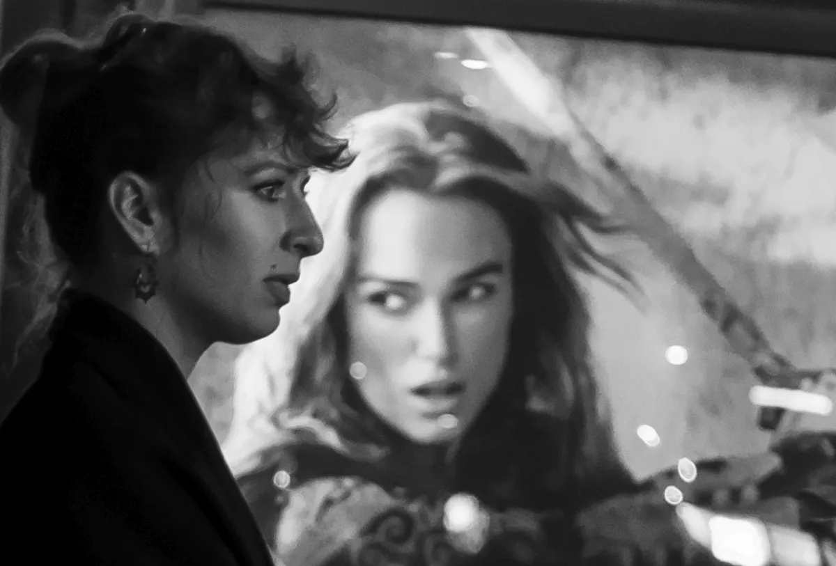Woman in profile passing a giant billboard face reflected in glass